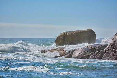 复制汹涌的大海的空间，汹涌的潮汐和汹涌的波浪，强风撞击在海滩上的大巨石上，背景是清澈的蓝天。