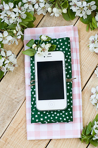 白色智能手机躺在木制背景上，周围环绕着鲜花。