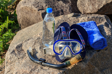 带水的瓶子、毛巾、人字拖、潜水面罩和石头上的通气管