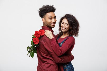 情侣概念-年轻的非洲裔美国夫妇互相拥抱，手捧浪漫的红玫瑰。