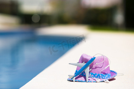 夏季游泳池附近的飞机模型和草紫色帽子