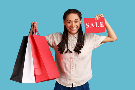劲暴低价摄影照片_女人拿着购物袋，出示销售卡，在商场里宣传低价。