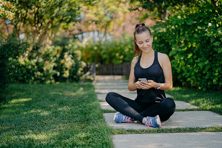 运动型女性休息一下，检查消息和通知，分享有关身着运动服的户外健身内容，在积极的有氧运动训练后放松健康的生活方式