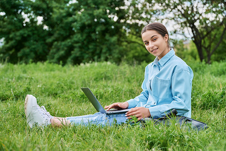 十几岁的女高中生坐在绿草上使用笔记本电脑