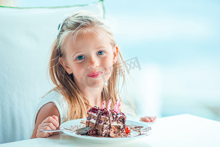 生日快乐庆祝蛋糕摄影照片_小女孩在户外咖啡馆用美味的蛋糕庆祝生日快乐