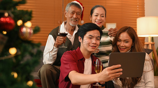 年轻夫妇使用数字平板电脑，在装饰着庆祝新年和圣诞节节日的客厅里与祖父母自拍