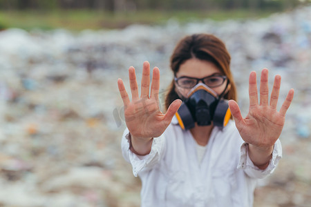 不在地球摄影照片_垃圾填埋场一名穿着防护呼吸服的妇女，双手举在前面，试图阻止地球的污染，并用手打出停车标志