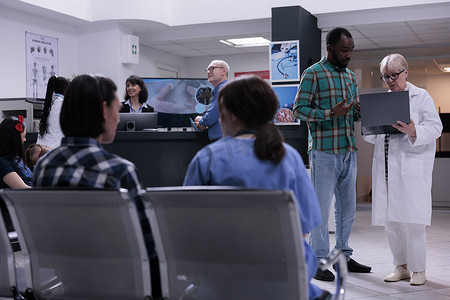 年长女医生拿着带有核磁共振扫描结果的笔记本电脑与私人诊所的非洲裔美国患者交谈