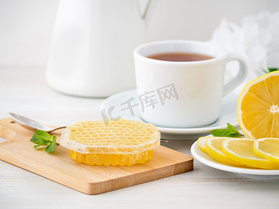 白杯，白木桌上蜂窝状的茶、柠檬片和蜂蜜，侧视