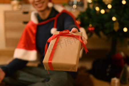 特写视图男人手拿着圣诞礼物，坐在装饰精美的房间里，灯光柔和