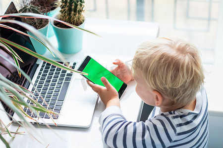 玩电脑看手机摄影照片_可爱的小男孩在看，在电话上玩，专注于色度键，手机的绿屏