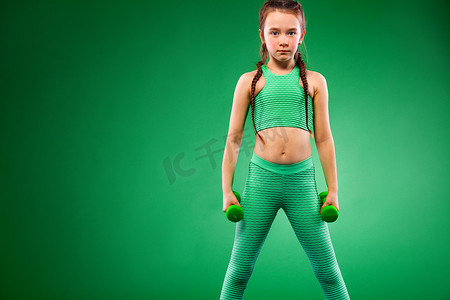 绿色背景下用哑铃做健身运动的小女孩