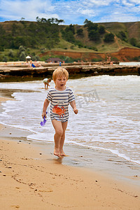 一个小男孩沿着海边的沙滩跑