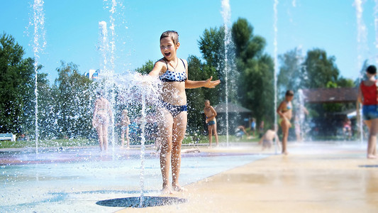 微笑、快乐的八岁女孩穿着泳衣，在街头城市喷泉、户外、公园、夏天、阳光明媚的假期里享受泼水的乐趣。