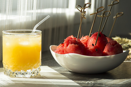 红色穗摄影照片_阳光下的木桌上放着鲜榨橙汁、甜西瓜甜点和成熟小麦的小穗。