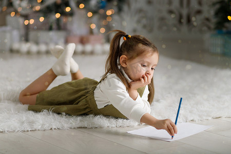 舒适的圣诞室内可爱的小女孩在圣诞树的背景下给圣诞老人写信
