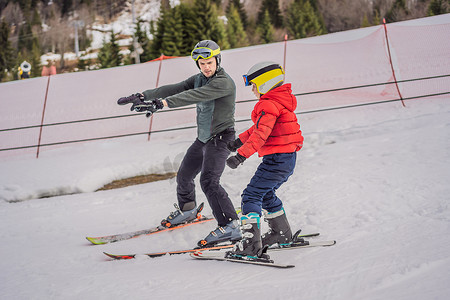 冬天的大山摄影照片_男孩在冬天在斜坡上学习滑雪、训练和听他的滑雪教练