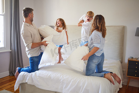 家庭枕头大战，在父母的卧室里，孩子们幸福地微笑。