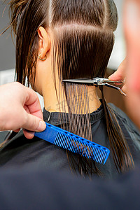 剪头发摄影照片_美容院里，男理发师用剪刀和梳子给女顾客剪头发。