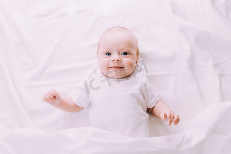 躺着睡觉的婴儿摄影照片_婴儿躺在他的婴儿床里，看着相机。
