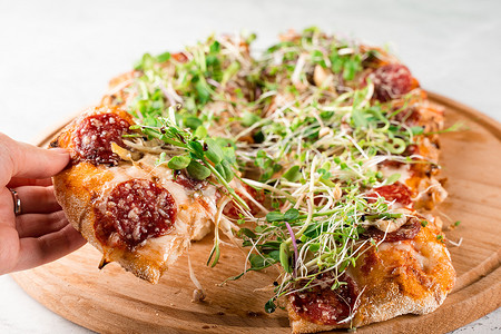 Pinsa romana 配意大利腊肠、奶酪、蘑菇，在白色背景的木板上装饰着微绿色植物。