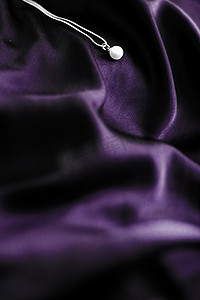 深紫色丝绸背景上的豪华白金珍珠项链，假日魅力珠宝礼物