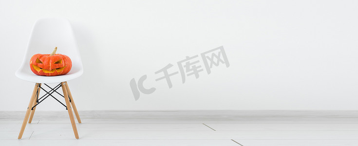 banner蔬菜摄影照片_Banner Jack-o-lantern 在白色现代椅子上雕刻南瓜，浅色墙壁背景上有复制空间、秋季和万圣节家居装饰