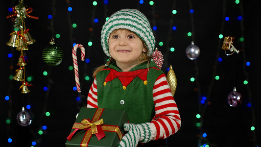 穿着圣诞精灵圣诞老人助手服装的孩子拿着带丝带的礼物惊喜礼盒