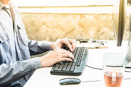在家庭办公室的台式电脑键盘上打字的男性手的特写