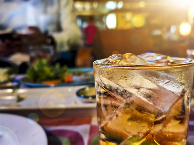 杯在冰上的威士忌酒与瓶在桌子木酒吧背景上。