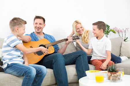 快乐的白人家庭在舒适的现代家中微笑、弹吉他和唱歌