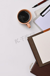 过硬摄影照片_一杯热咖啡、笔记本和剪贴板放在白桌上。