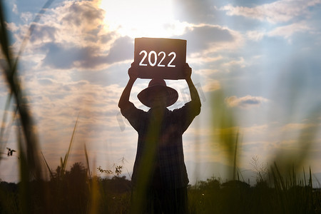 一位资深农民在日落时站在稻田里，举着 2022 年新年标志的剪影。