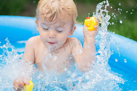 可爱的小孩在庭院里的蓝色街边泳池里和鸭子一起洗澡。