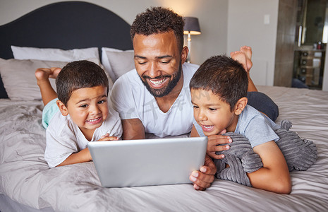 有趣的卧室摄影照片_快乐，父亲和孩子们在家里的卧室里看数字平板电脑上的娱乐节目。
