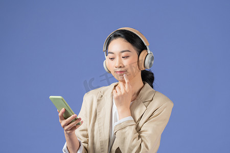 开朗漂亮的年轻亚洲女性拿着手机，用紫色背景中突显的无线耳机听音乐