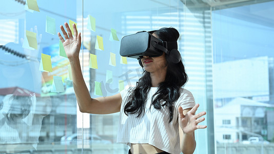 现代发明摄影照片_年轻的女性开发人员戴着虚拟现实眼镜，在现代办公室与数字界面交互。