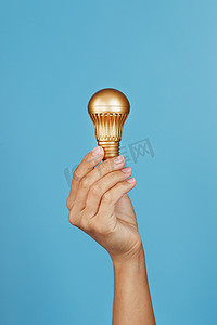协助的手摄影照片_蓝色背景中手持金灯泡，作为思想和协助的概念