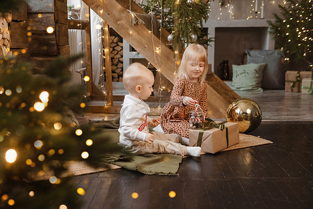 友谊装饰摄影照片_弟弟和妹妹在圣诞节前夕在为新年假期装饰的漂亮房子里玩耍。
