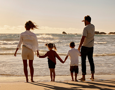 空闲时间摄影照片_白人父母带着儿子和女儿在海滩上享受空闲时间的背影。