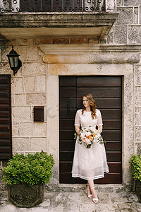 拿着花束的新娘站在一座老石屋的门口