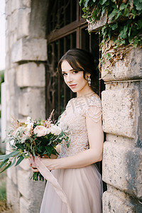 爱心彩石摄影照片_带着花束的新娘站在石栅栏的伪造门前