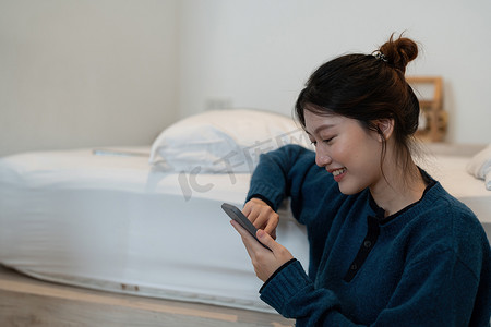 快乐的亚洲女性手使用智能手机打字，在卧室的聊天框中聊天，社交媒体制作概念。