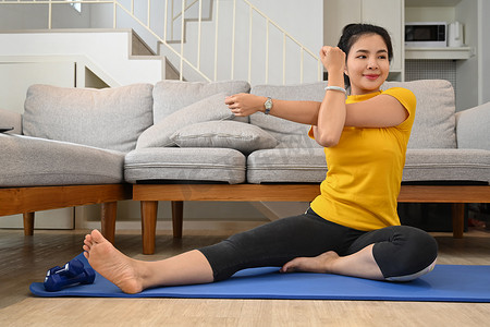 身体平衡摄影照片_美丽的女人在公寓里伸展双臂锻炼身体