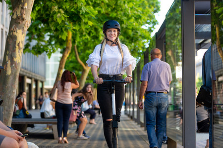 时尚时尚的青少年，美丽的金发女孩在城市环境中骑着公共租赁电动滑板车。