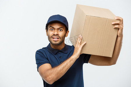 送货概念 — 严肃的非洲裔美国送货员拿着盒子包裹，表现出愚蠢的攻击性表情的肖像。