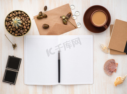 白色开放式记事本、牛皮纸信封、咖啡和仙人掌放在米色木桌上的锅里