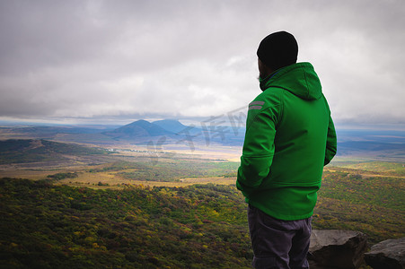 秋天山顶上的一位男游客背对着镜头站着，看着云中的山脊
