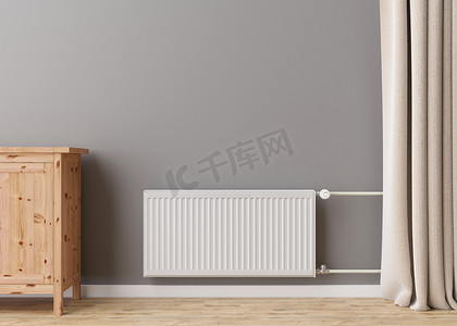 现代房间灰色墙上带恒温器的白色暖气散热器。