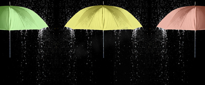 黑色背景雨滴下的三色雨伞